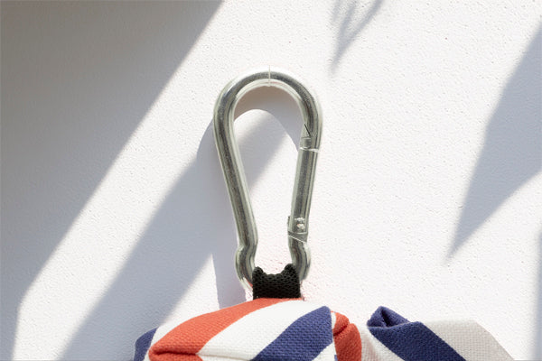 Gros plan sur le mousqueton de la pochette sac à crottes Pawtriote. Le motif du harnais reprend les rayures tricolores avec un rappel des couleurs de la France