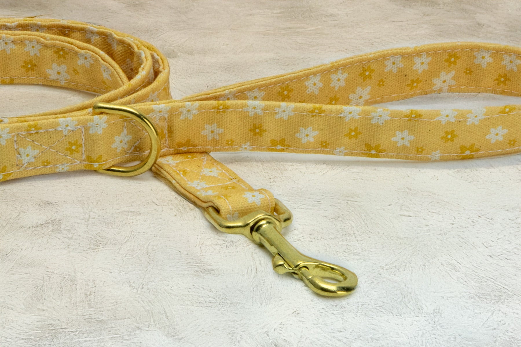Gros plan sur l'anneau en D et le mousqueton de la laisse Peachy Daisies. Le motif de la laisse représente des marguerites blanches et jaunes sur un fond couleur pêche.