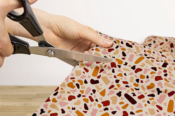 Gros plan sur la coupe aux ciseaux du tissu Pawpino, motif marbré terrazzo aux tons rosés.
Design made in France et tissu OEKO-TEX®