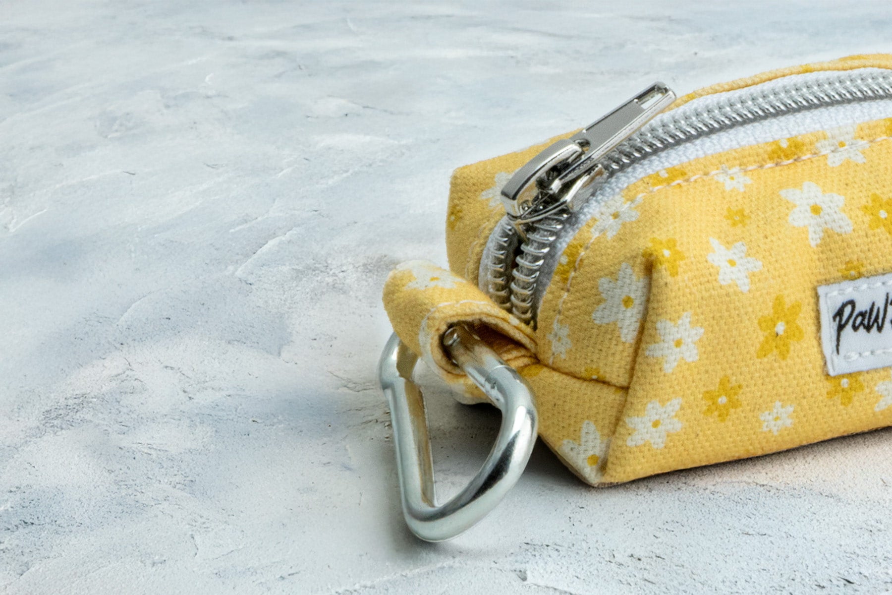 Gros plan sur le mousqueton et la fermeture éclaire de la pochette sac à crottes Peachy Daisies. La pochette possède un motif de marguerites blanches et jaunes sur fond couleur pêche.