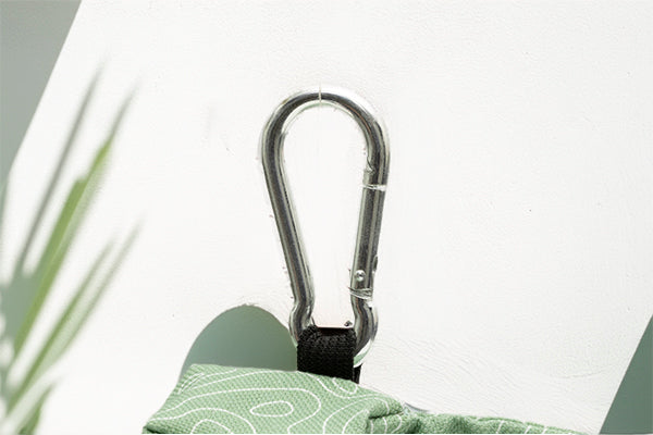 Gros plan sur le mousqueton de la pochette sac à crottes Topo. Le motif Topo reprend le design géométrique abstrait des cartes de montagnes, avec des lignes blanches sur un fond vert