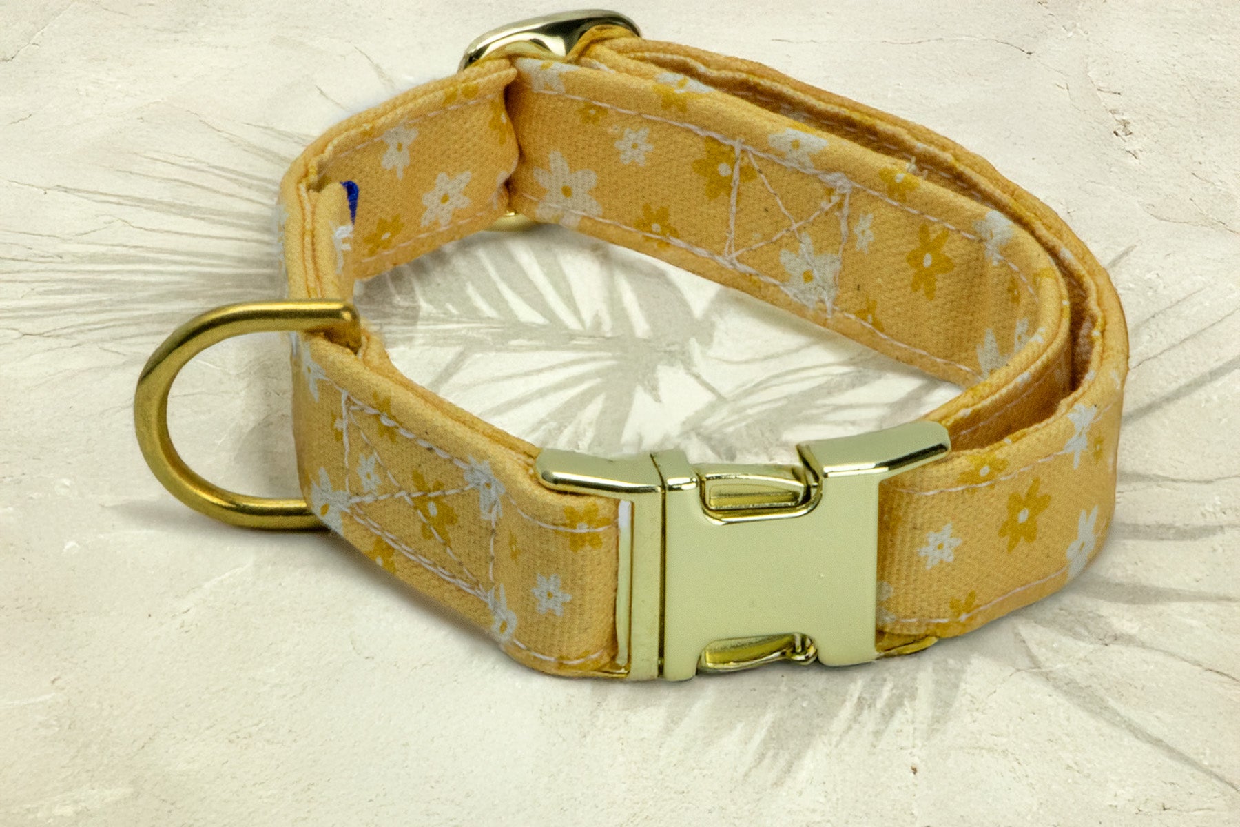 Gros plan sur les boucles du collier pour chien Peachy Daisies. Les boucles clips, anneaux en D et boucles de reglages sont disponibles couleur or ou argent. Le collier possède un motif marguerites blanches et jaunes sur un fond couleur pêche. 