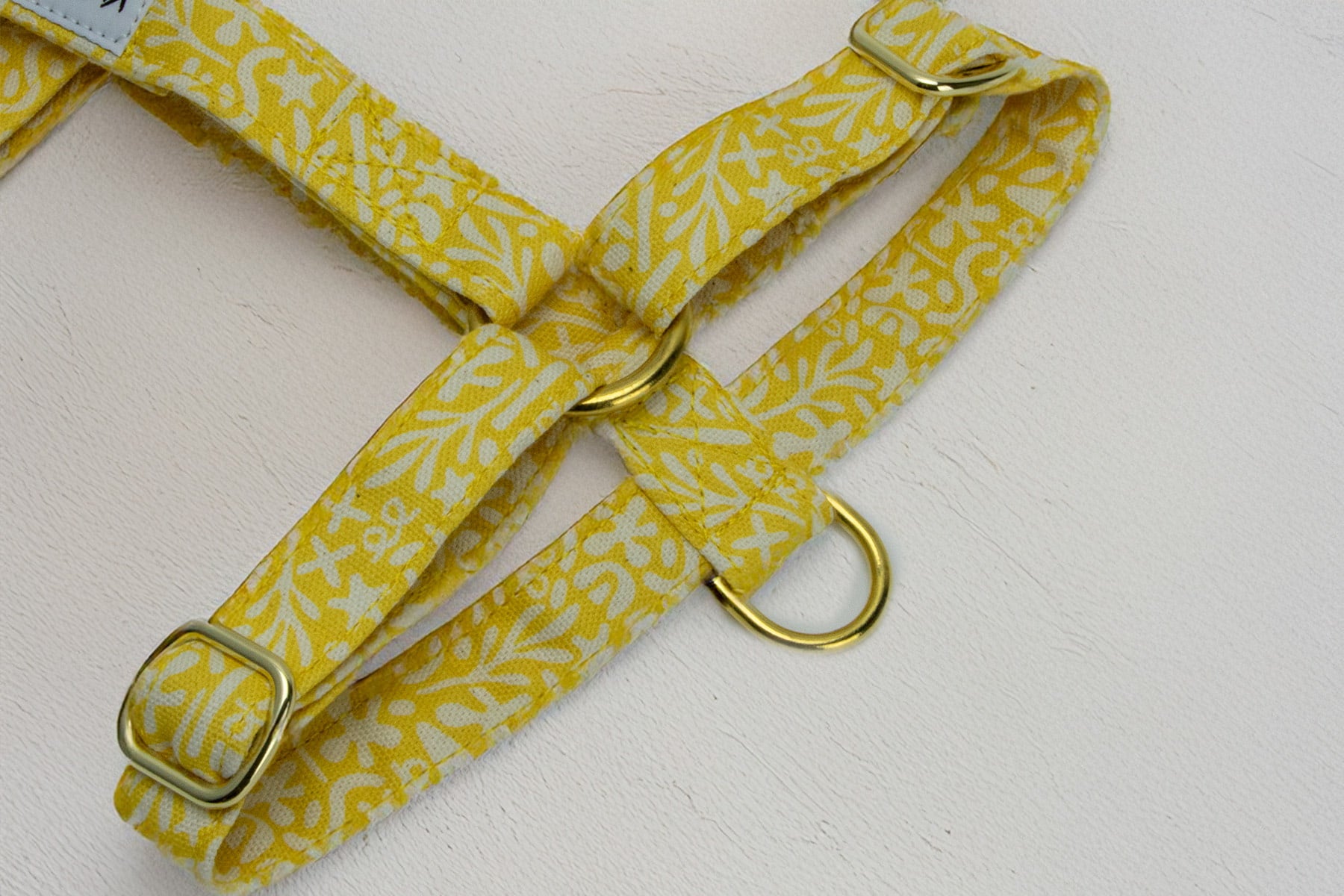Focus sur les boucles de reglages et anti traction du harnais pour chien Seaside. Le harnais possède un motif marin abstrait blanc sur un fond jaune solaire. Les boucles sont de couleur or, mais peuvent également être en argent. 