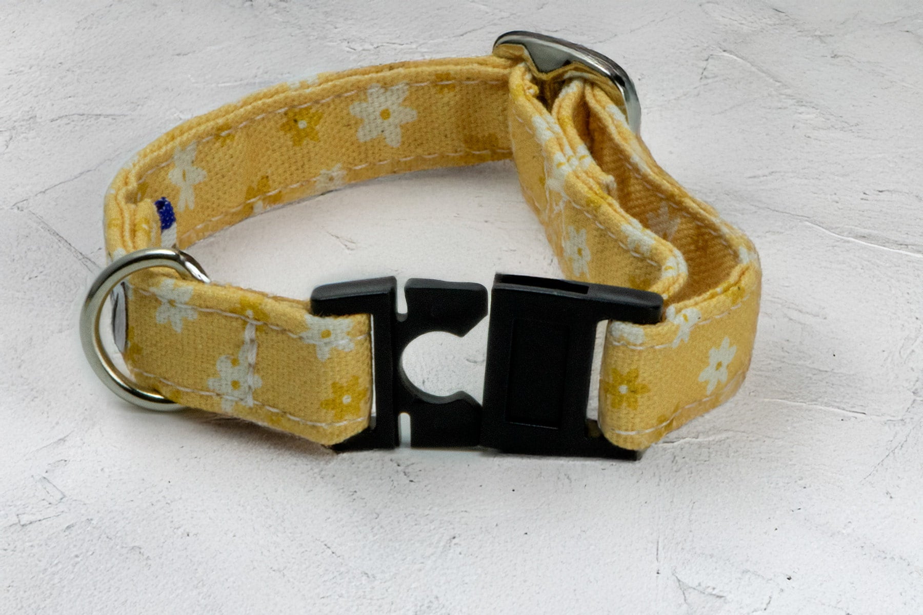 Focus sur la boucle du collier pour chat Peachy Daisies. Le collier possède une boucle anti-étranglement pour la sécurité du chat. Le collier est avec un motif marguerites blanches et jaunes sur un fond couleur pêche. 