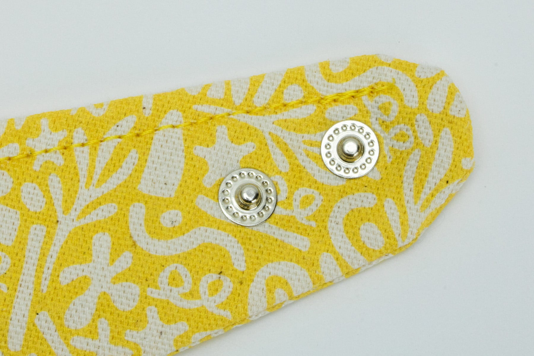 Boutons pressions sur le bandana Seaside pour chien et chat de Pawpix. Les boutons pressions permettent de régler au mieux le bandana. Le bandana possède un motif marin abstrait blanc sur un fond jaune solaire. 