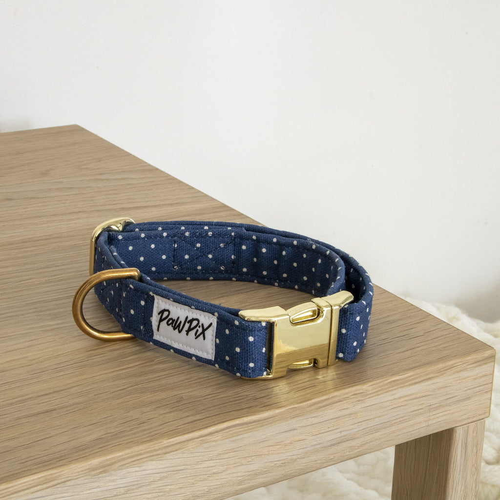 Collier pour chien Polaris. Design bleu marine avec des pois blanc. Le collier est posé sur une table dans une ambiance cosy. 