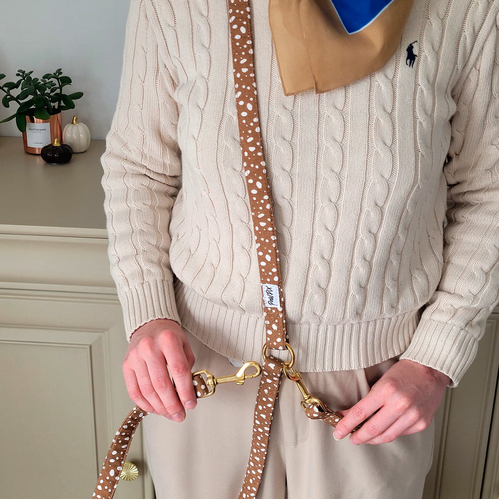 Laisse multi positions pour chien Freckles portée en bandoulière, ses boucles en or et son motif tacheté blanc sur fond marron