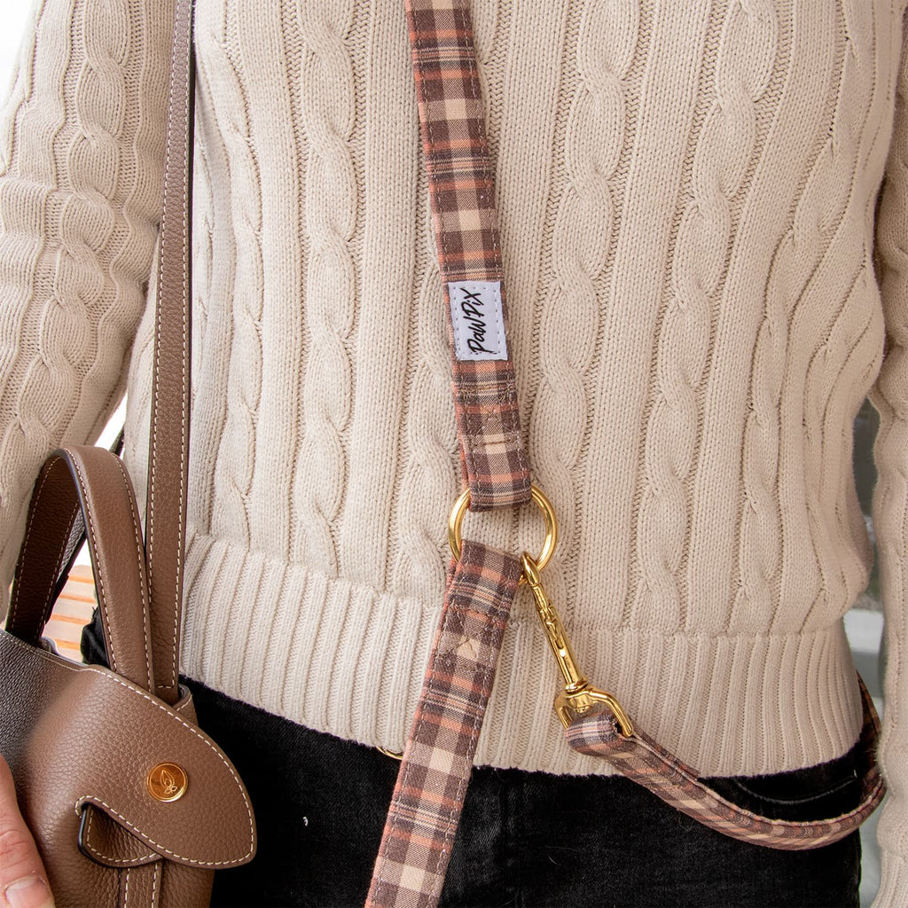 Laisse multi positions Scotty et ses boucles en or portée en bandoulière. Motif tartan écossais marron et orange 