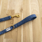 Laisse Polaris. Design bleu marine avec des pois blanc avec un focus sur le mousqueton couleur doré et la anse de la laisse