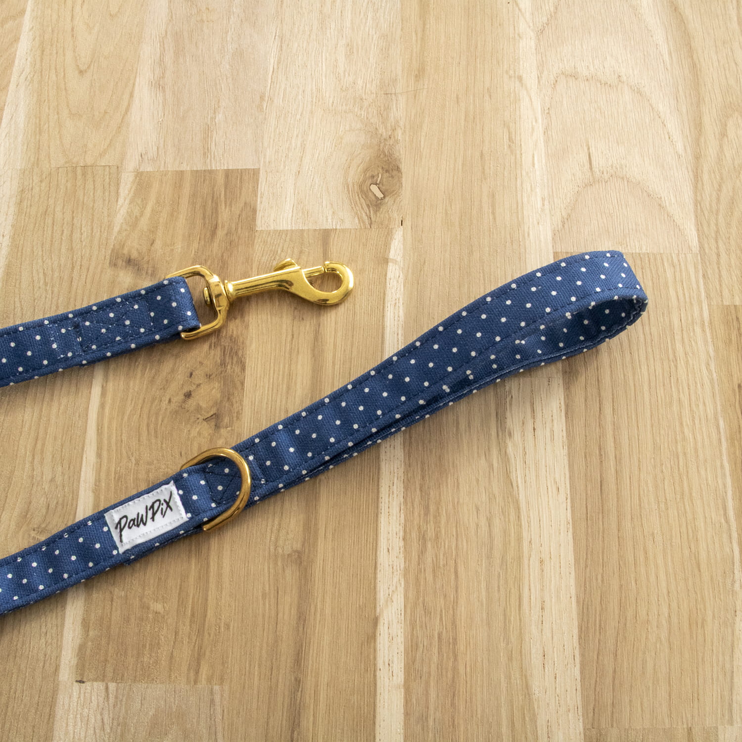 Laisse Polaris. Design bleu marine avec des pois blanc avec un focus sur le mousqueton couleur doré et la anse de la laisse