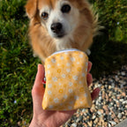 Gros plan de la mini sacoche pour chien Peachy Daisies ouverte devant un petit chien. Motif fleurs blanches et jaunes sur fond couleur pêche. 