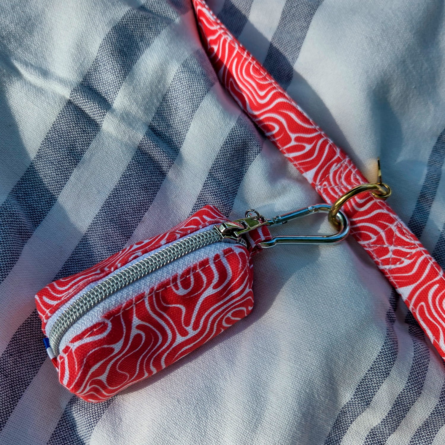Vue rapprochée de la pochette sacs à crottes Cherry de Pawpix accrochée à la laisse Cherry de Pawpix. Les deux produits présentes un motif rouge et blanc wavy. 
