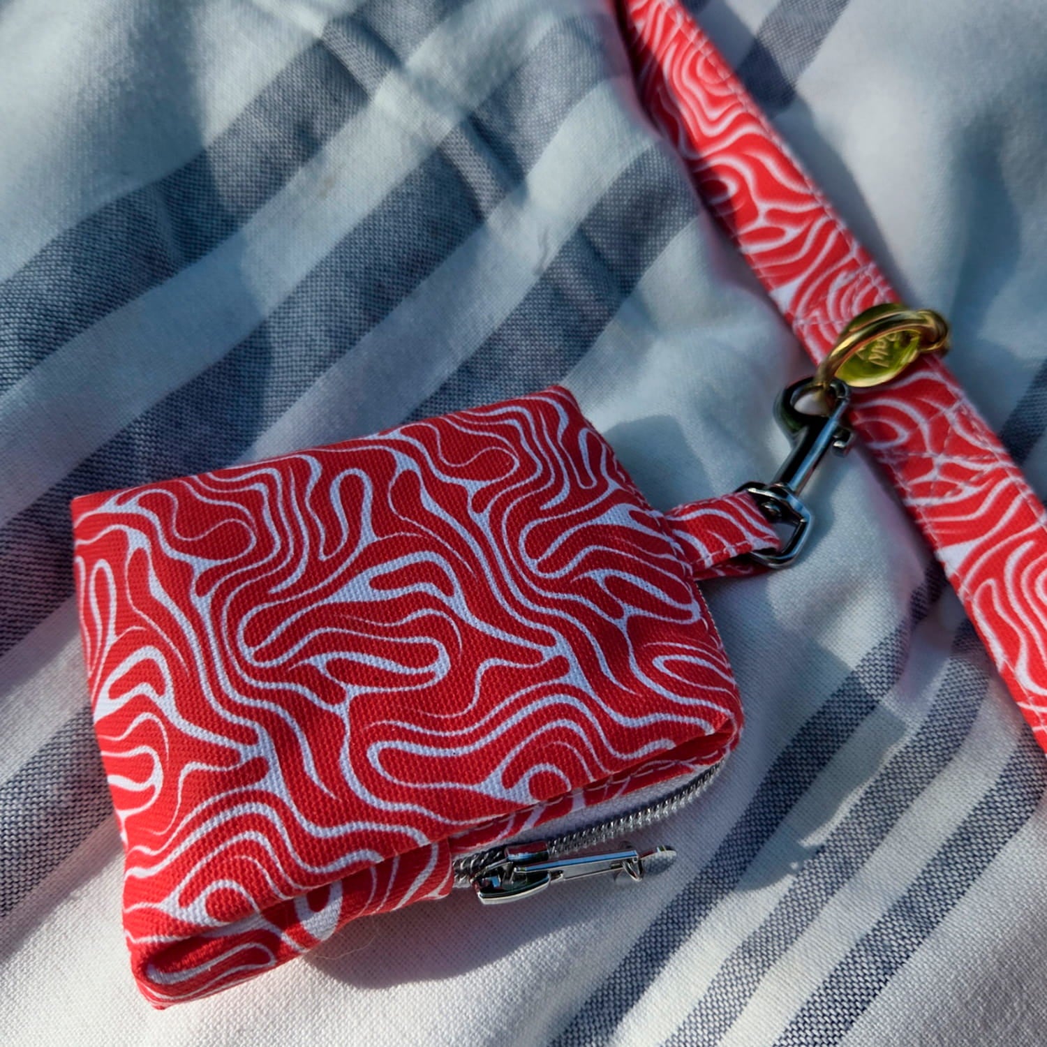 Vue rapprochée de la mini sacoche Cherry de Pawpix accrochée à la laisse Cherry de Pawpix. La laisse et la mini sacoche présente un motif rouge et blanc wavy