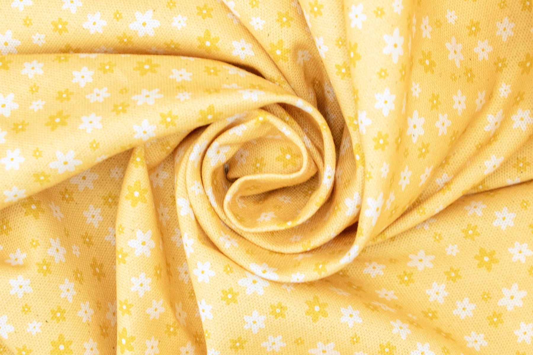 Gros plan sur le tissu Peachy Daisies de la collection été de Pawpix. Le tissu présente des marguerites blanches et jaunes sur un fond couleur pêche. 