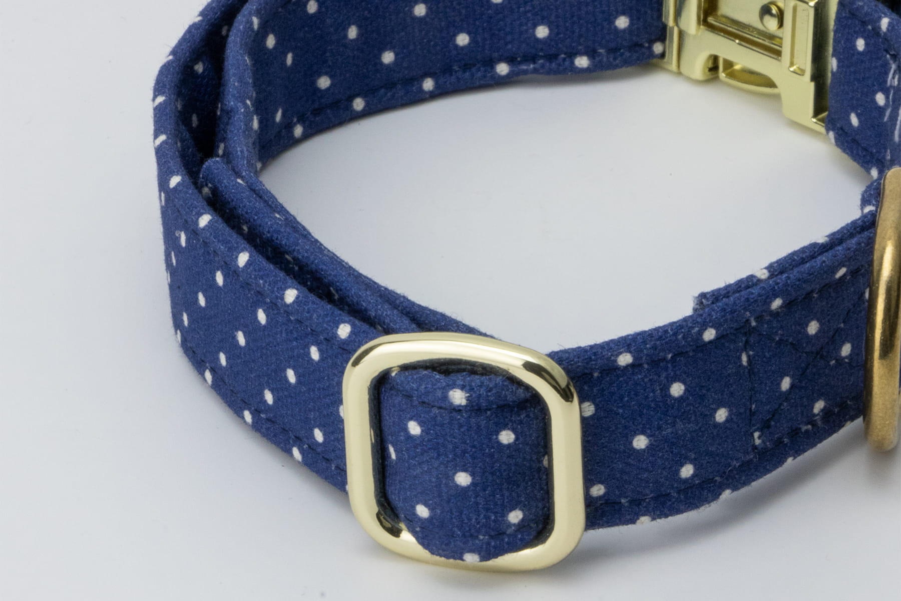 Gros plan sur la bouclerie du collier pour chien Polaris. Motif bleu marine avec des pois blancs et une bouclerie couleur or 