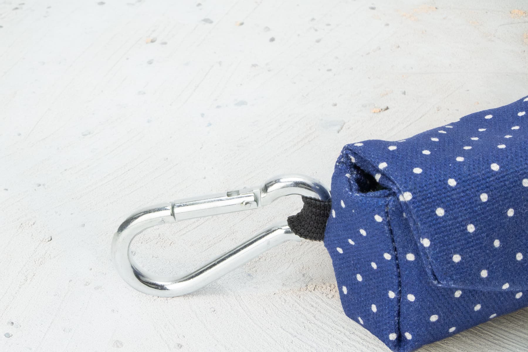 Gros plan sur le mousqueton de la pochette sacs à crottes Polaris. La boucle est en acier et le design de la pochette est bleu marine avec des pois blancs